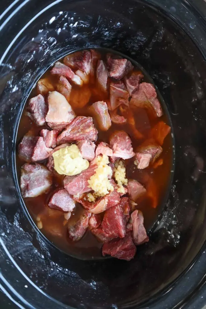 beef broth, minced garlic, Dijon mustard, salt and pepper on top of stewing beef chunks in a Crock Pot