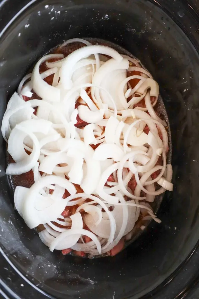 onion slices on top of stewing beef in a slow cooker
