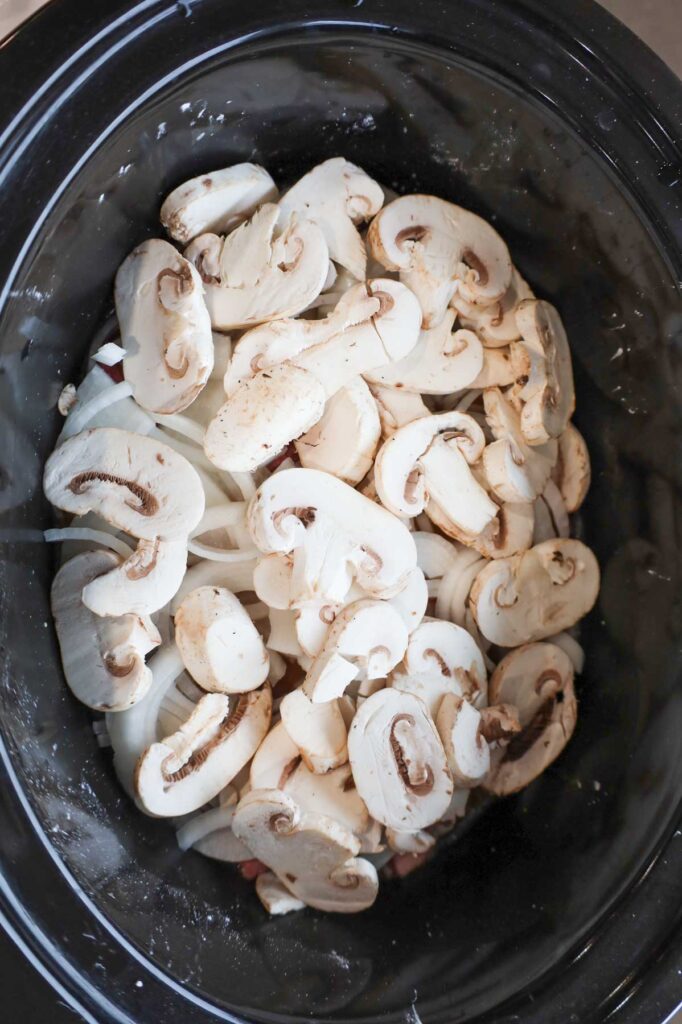 sliced mushrooms and sliced onions on top of stewing beef in a Crock Pot
