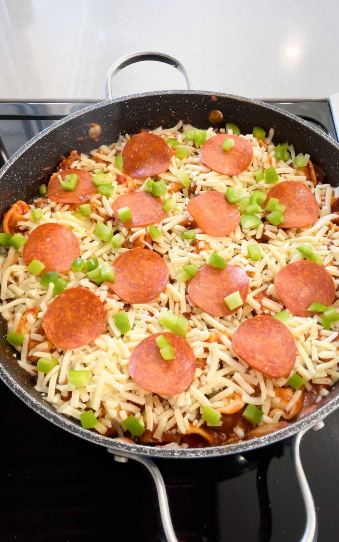 diced green peppers, pepperoni slices and mozzarella cheese on top of tortellini in a skillet.