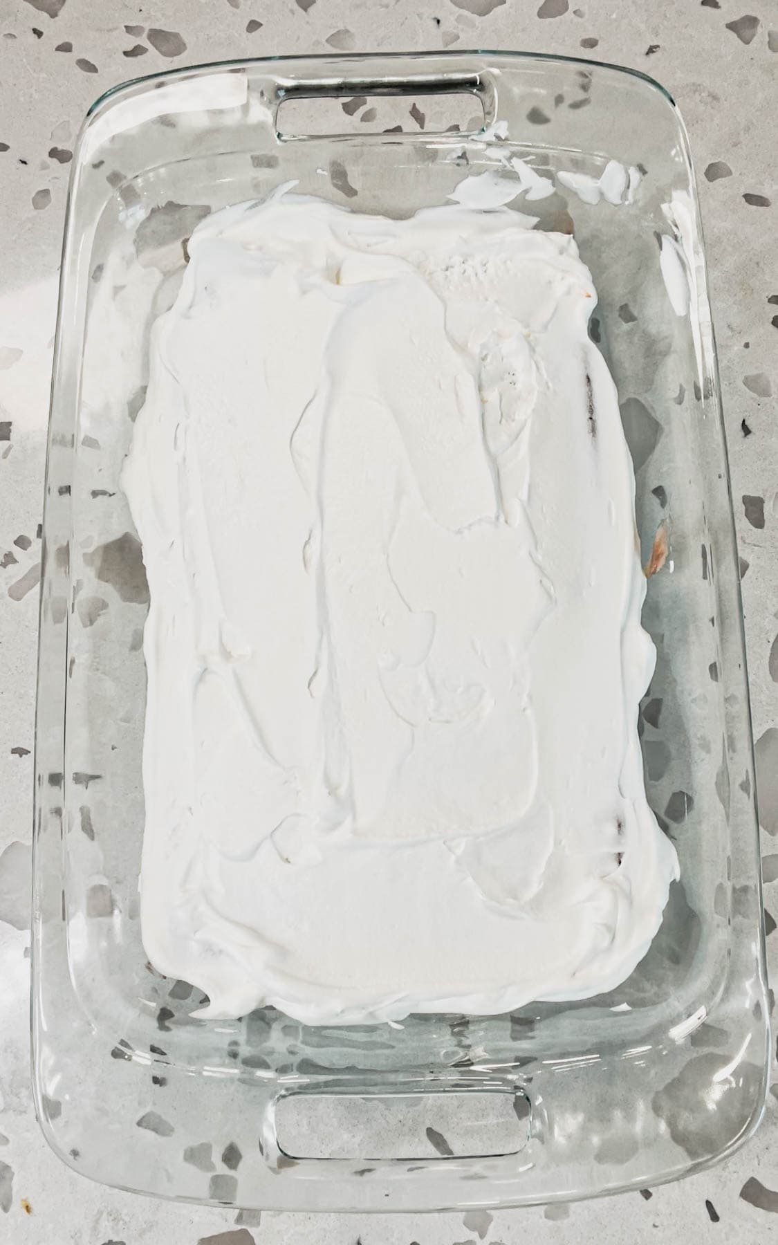 cool whip spread on top of ice cream sandwiches in a baking dish