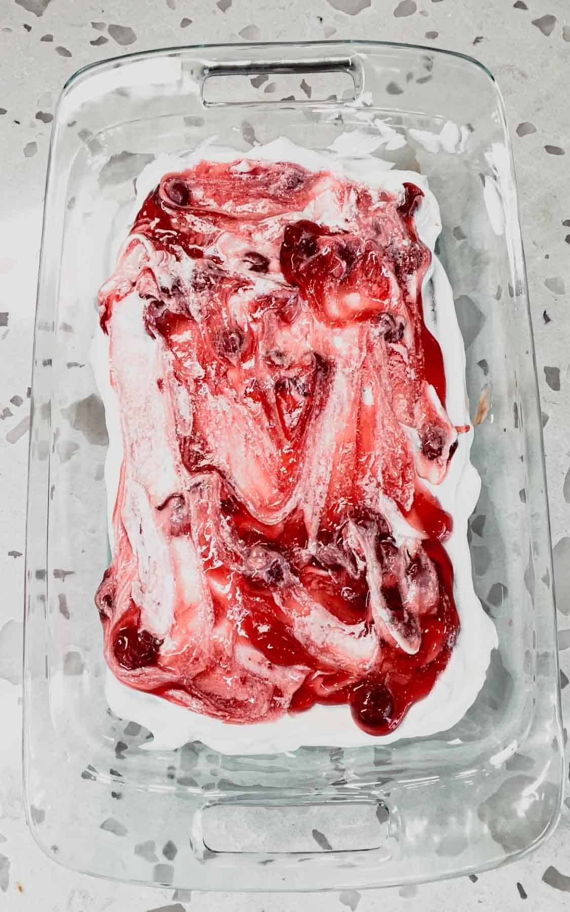 cherry pie filling on top of cool whip and ice cream sandwiches in a baking dish