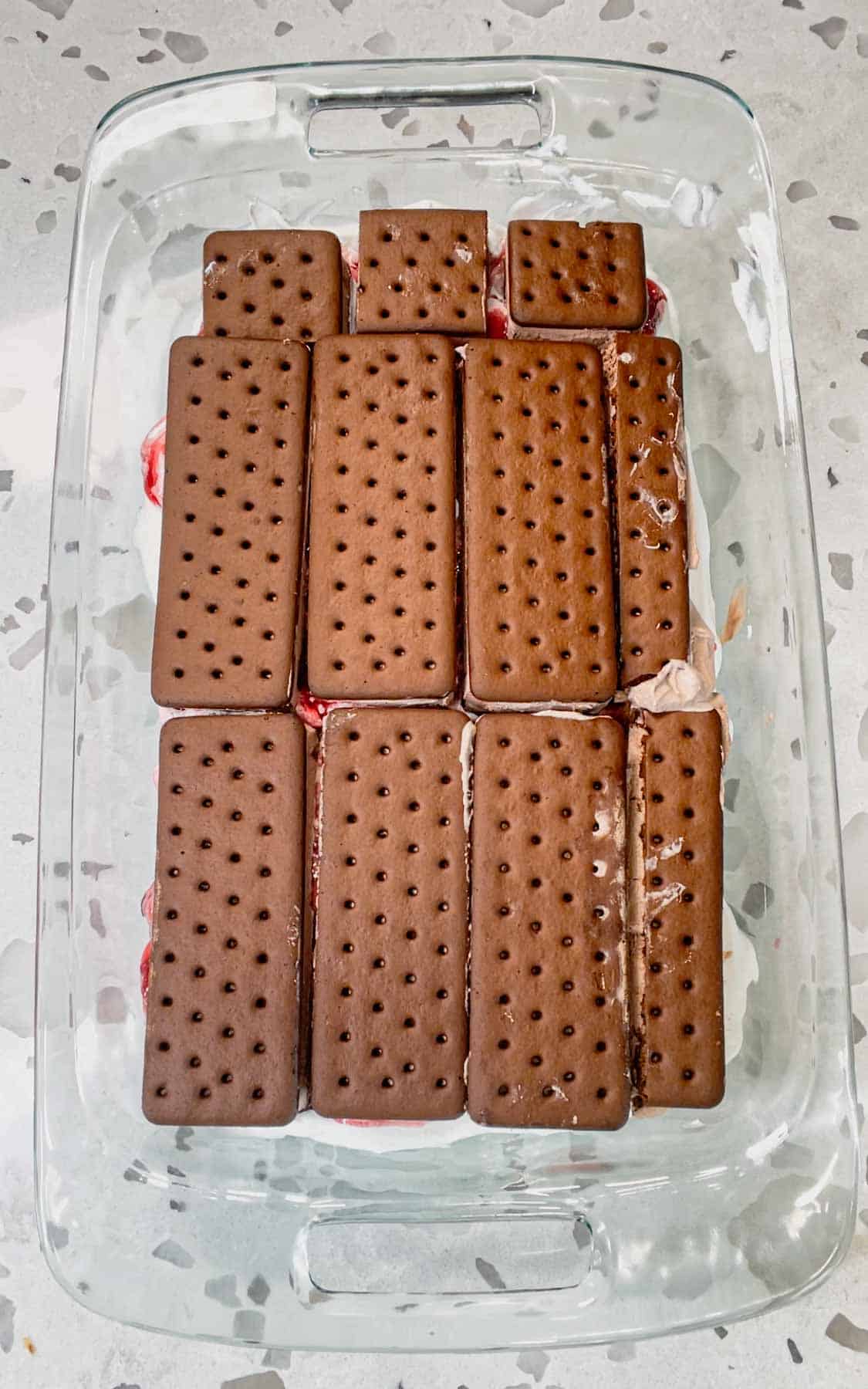 ice cream sandwiches on top of cool whip and cherry pie filling in a baking dish