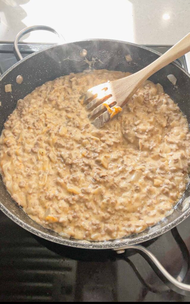 cheddar cheese stirred into creamy ground beef mixture in a skillet
