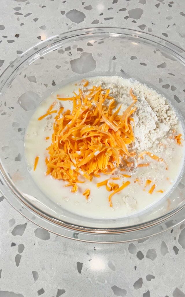 shredded cheddar cheese and milk added to bowl with cheddar bay biscuit mix