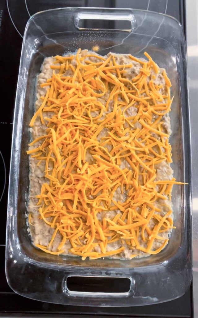 shredded cheddar cheese on top of creamy ground beef mixture in a baking dish