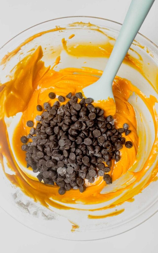 dark chocolate chips added to a mixing bowl with orange brownie batter