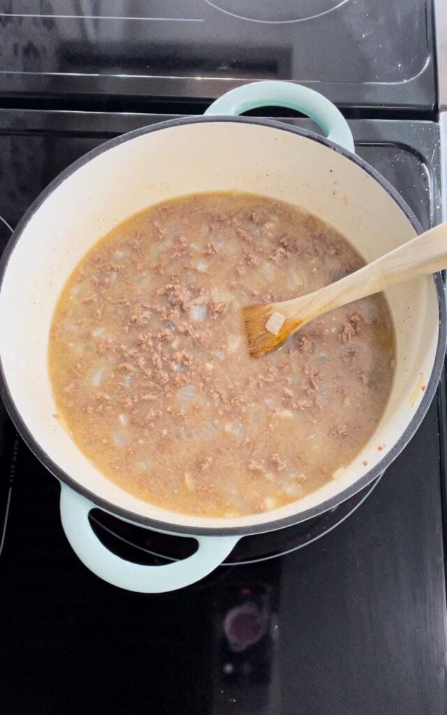 chicken broth being stirred with ground beef and flour mixture in a pot