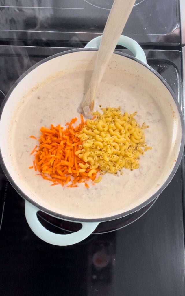 matchstick carrots and uncooked macaroni noodles added to cheeseburger soup in a pot
