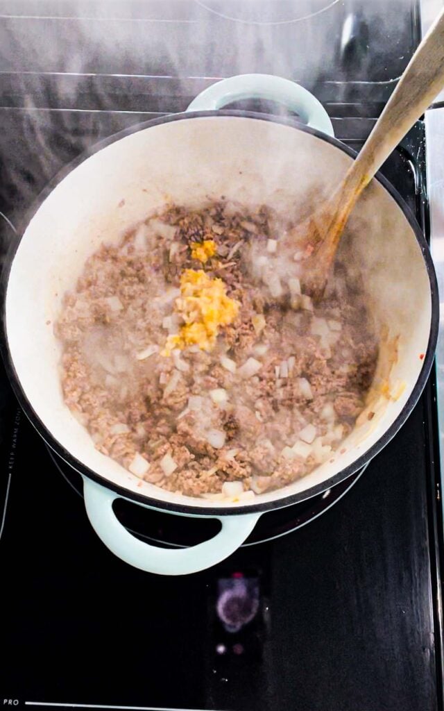 chopped garlic on top of cooked ground beef and onions in a dutch oven
