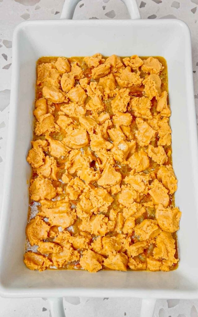 peanut butter cookie dough clumps over pecan pie filling in a baking dish