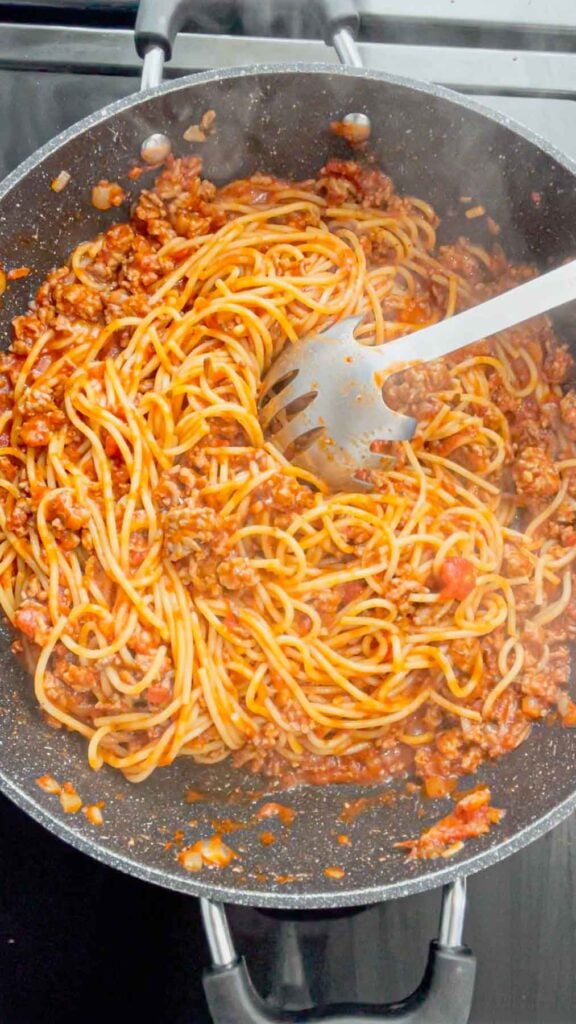 stirring spaghetti and ground beef and marinara mixture together in a skillet