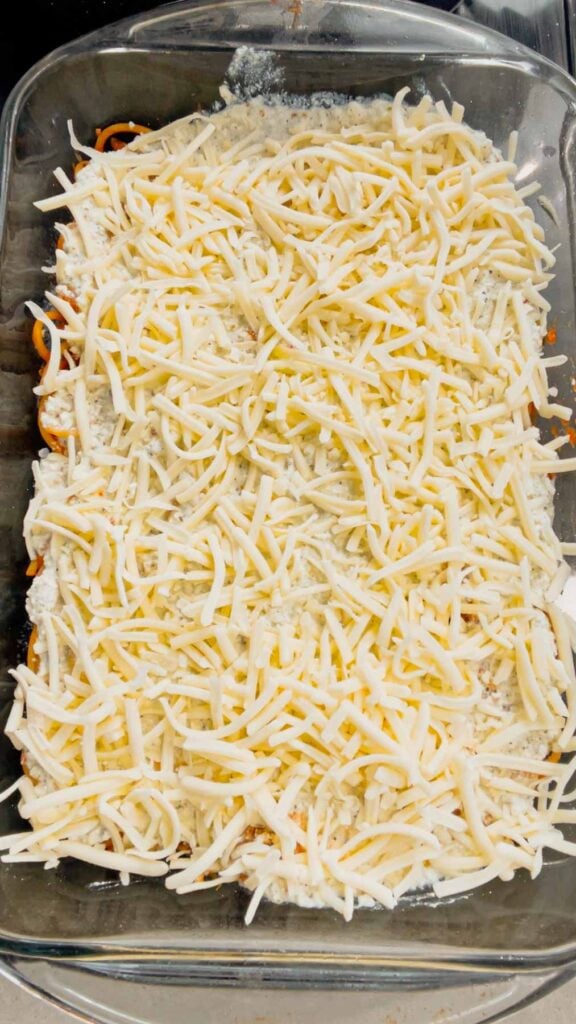 shredded mozzarella cheese on top of ricotta and spaghetti in a baking dish