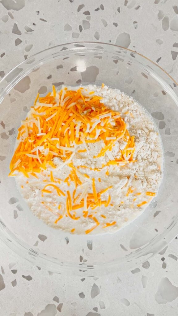 shredded cheddar, cheese, milk and biscuit mix in a bowl