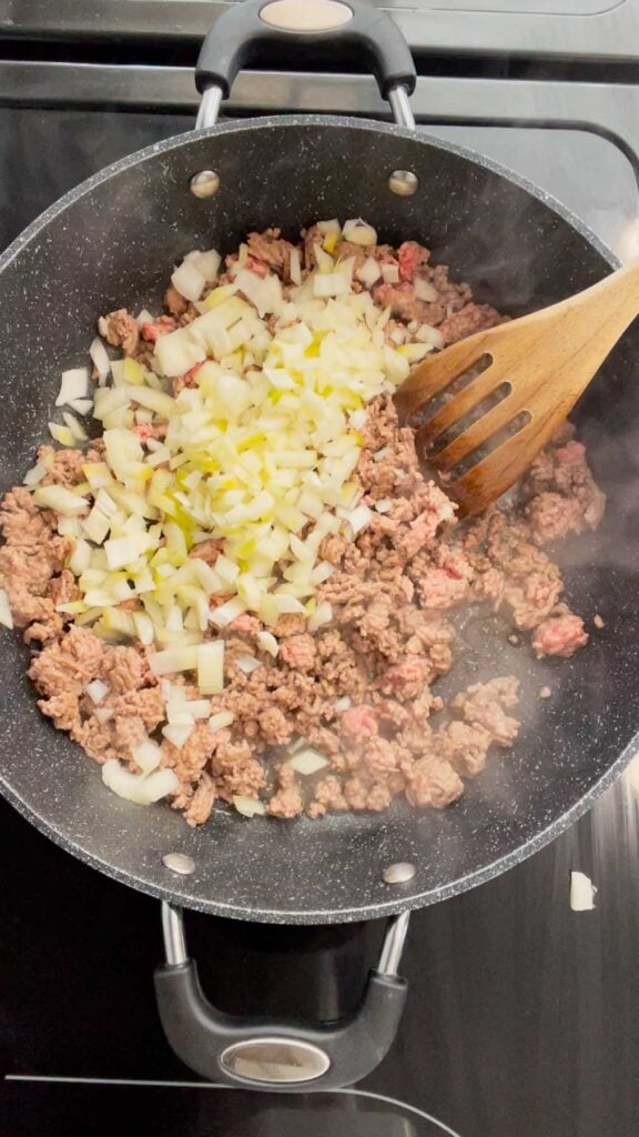 diced onions added to a skillet with crumbled ground beef