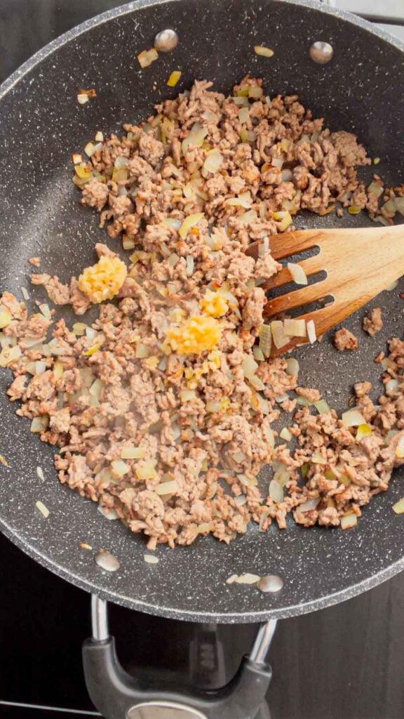 chopped garlic on top of cooked ground beef and diced onions in a skillet