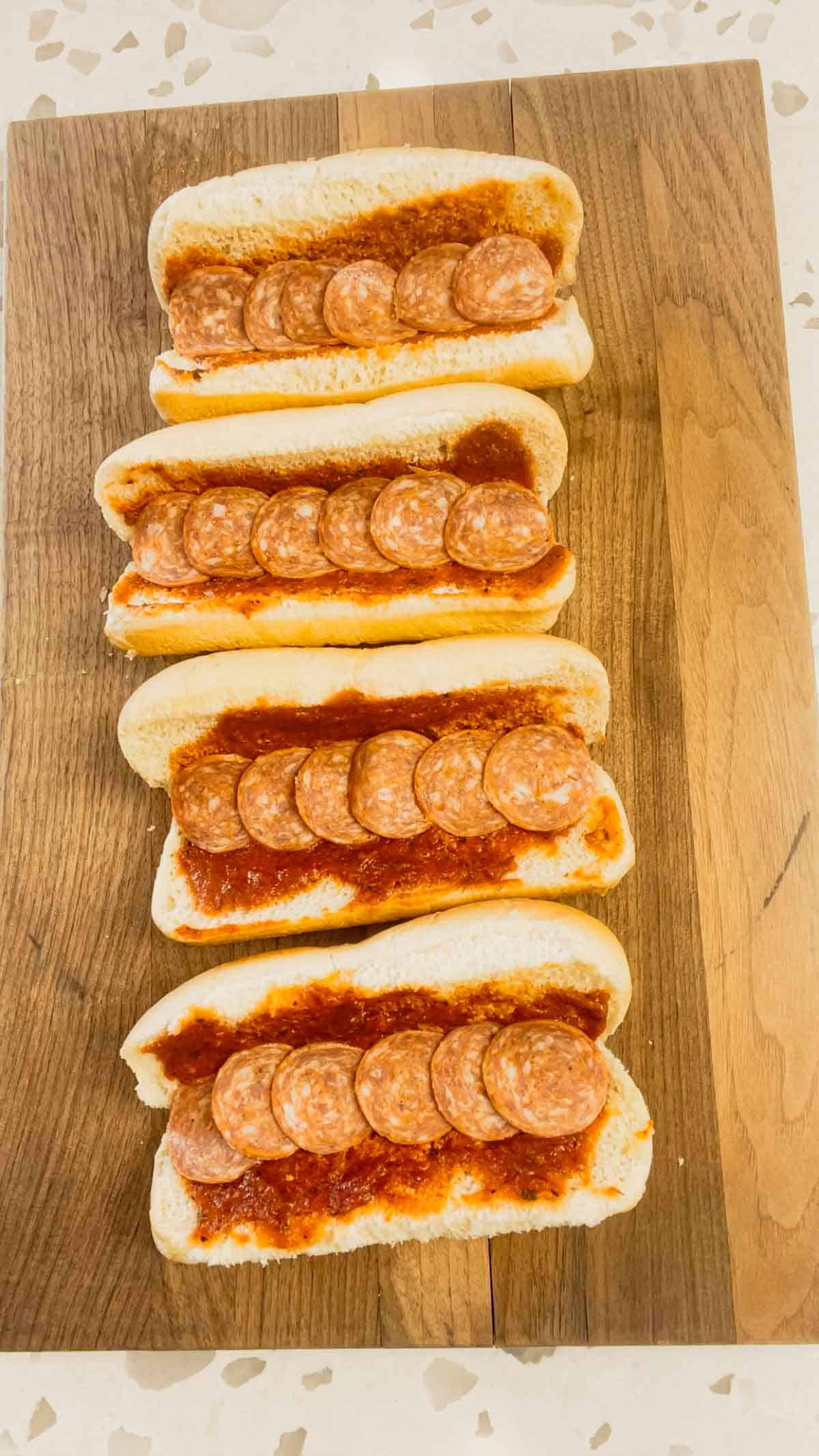 pepperoni slices in the bottom of hot dog buns spread with pizza sauce