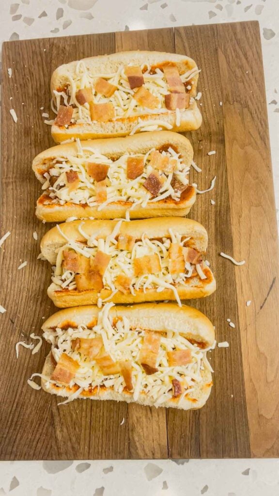 bacon pieces on top of mozzarella cheese on hot dogs