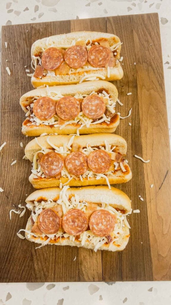 pepperoni slices and shredded mozzarella cheese on top of hot dogs