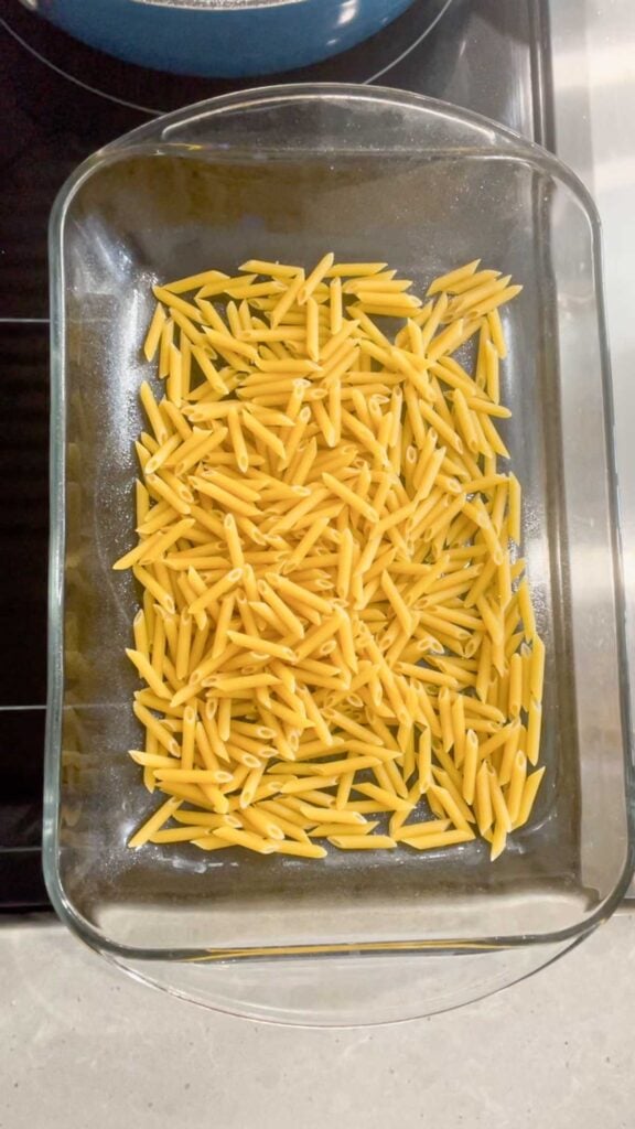 uncooked mini penne noodles in the bottom of a glass baking dish
