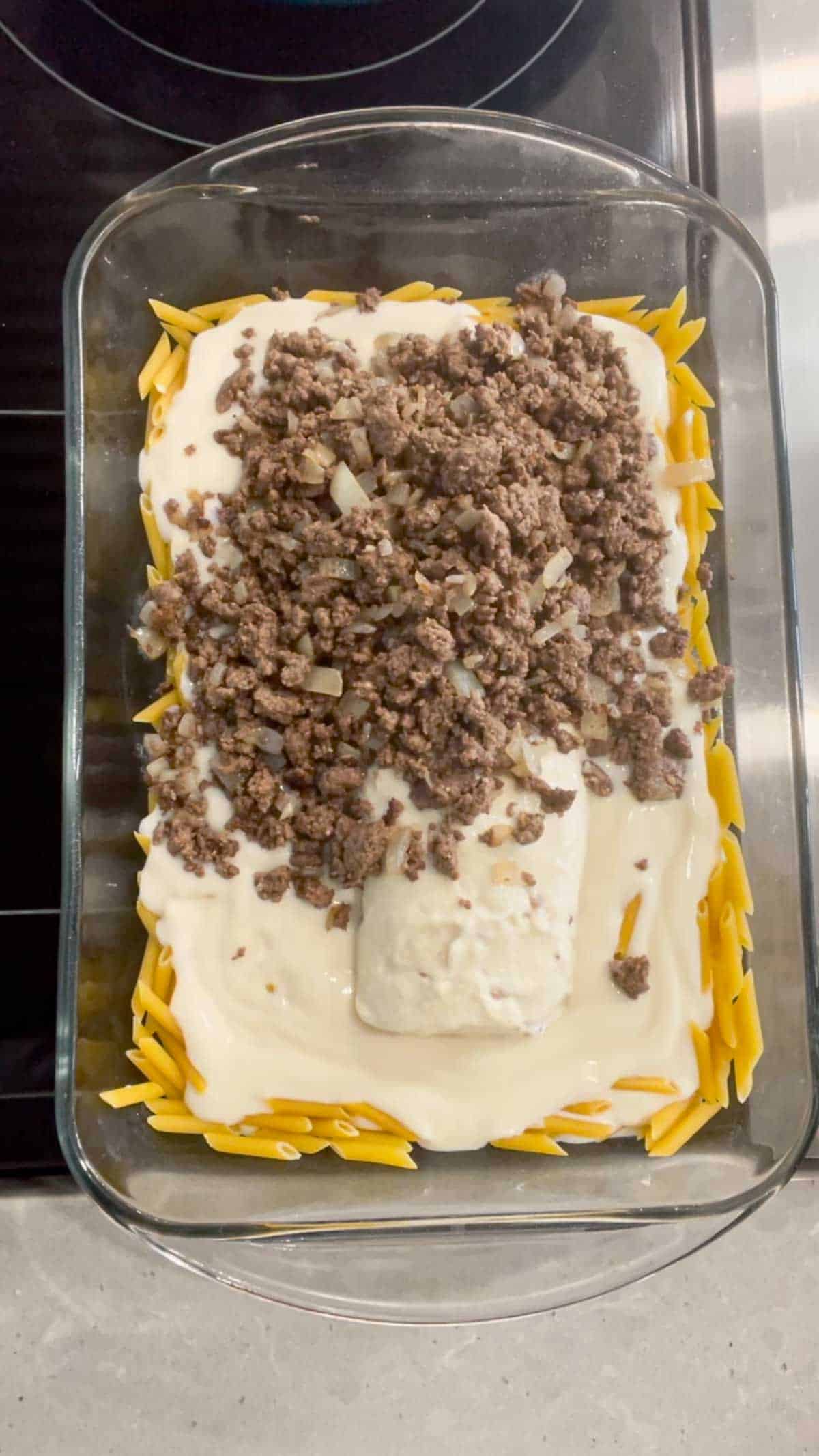 cooked ground beef, condensed cream of bacon soup and alfredo sauce on top of uncooked mini penne noodles in a baking dish