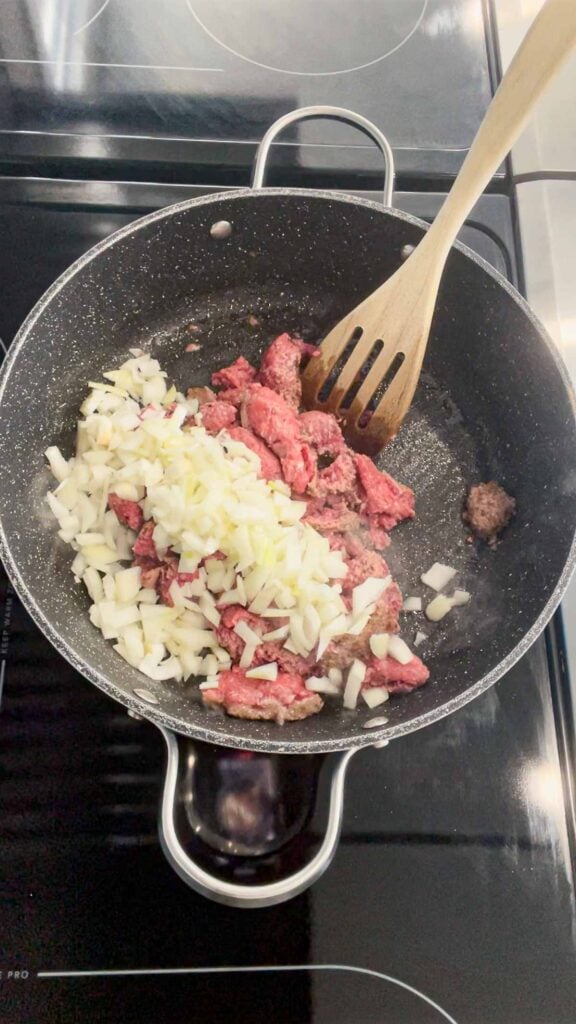 diced onions on top of ground beef in a skillet