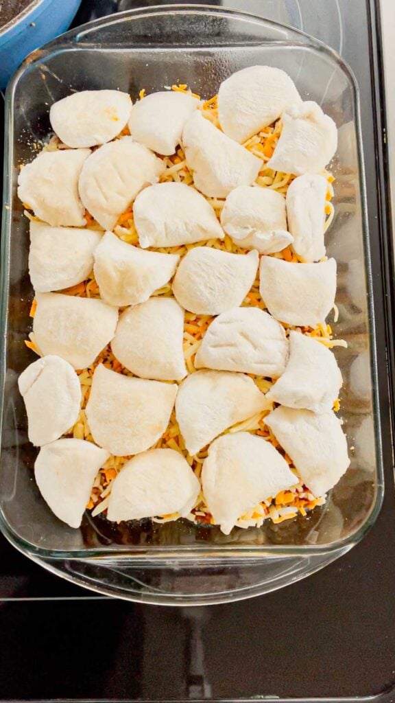 frozen pierogies on top of shredded cheese in a baking dish