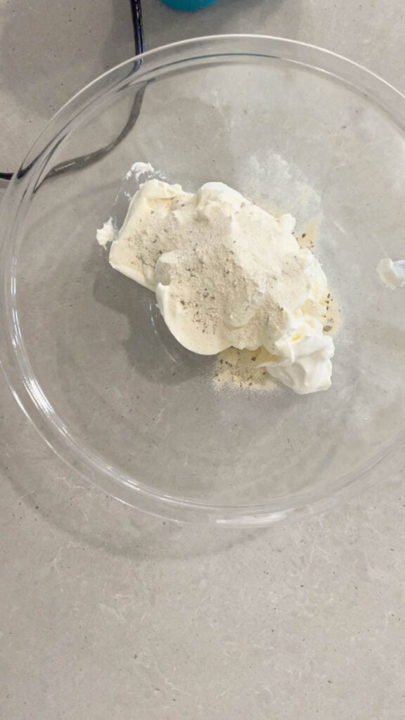 ranch dressing mix on top of sour cream and cream cheese in glass mixing bowl