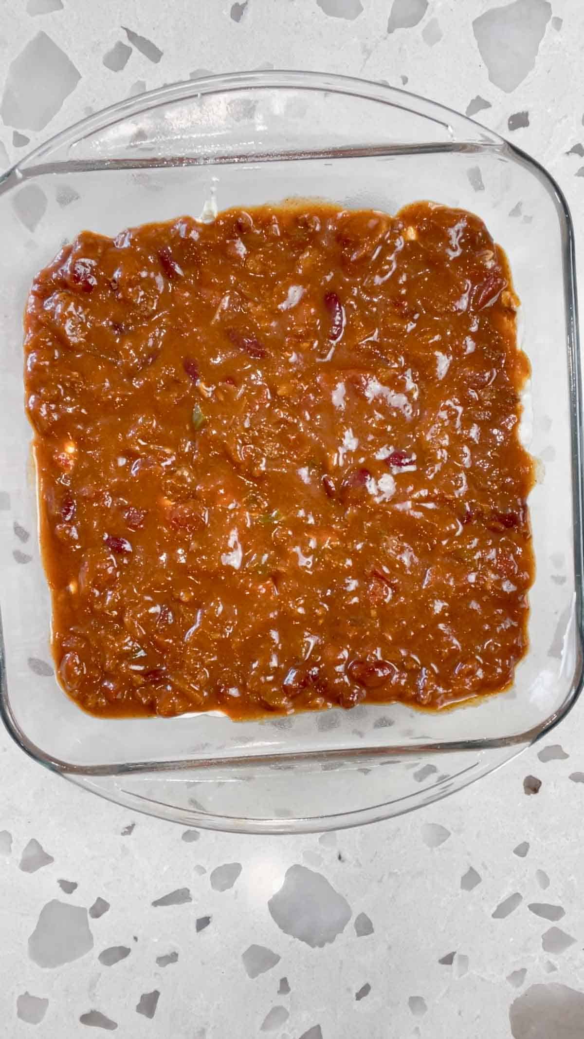 chili spread over cream cheese mixture in a square baking dish