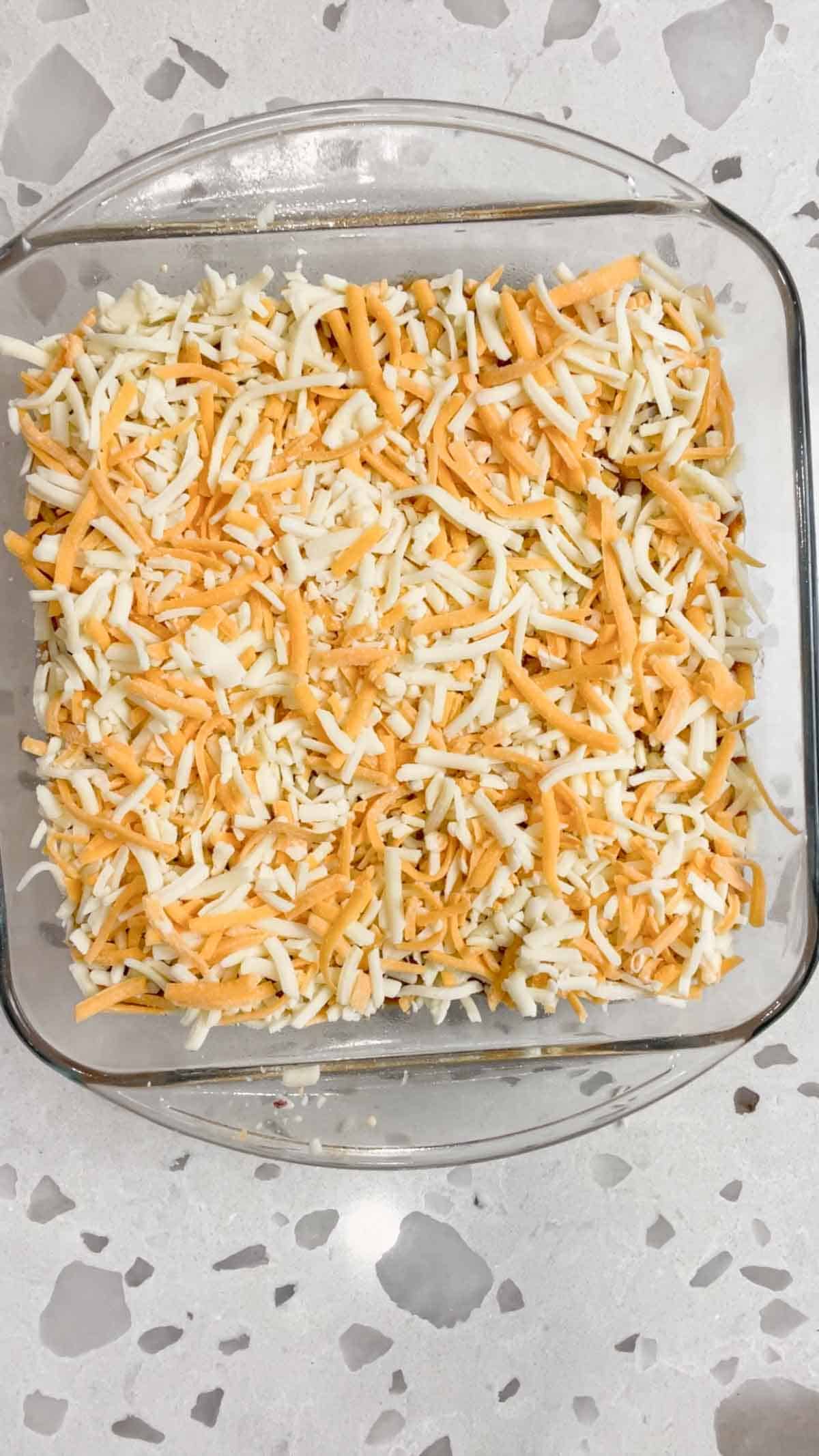 shredded nacho cheese on top of chili cream cheese dip in a glass baking dish