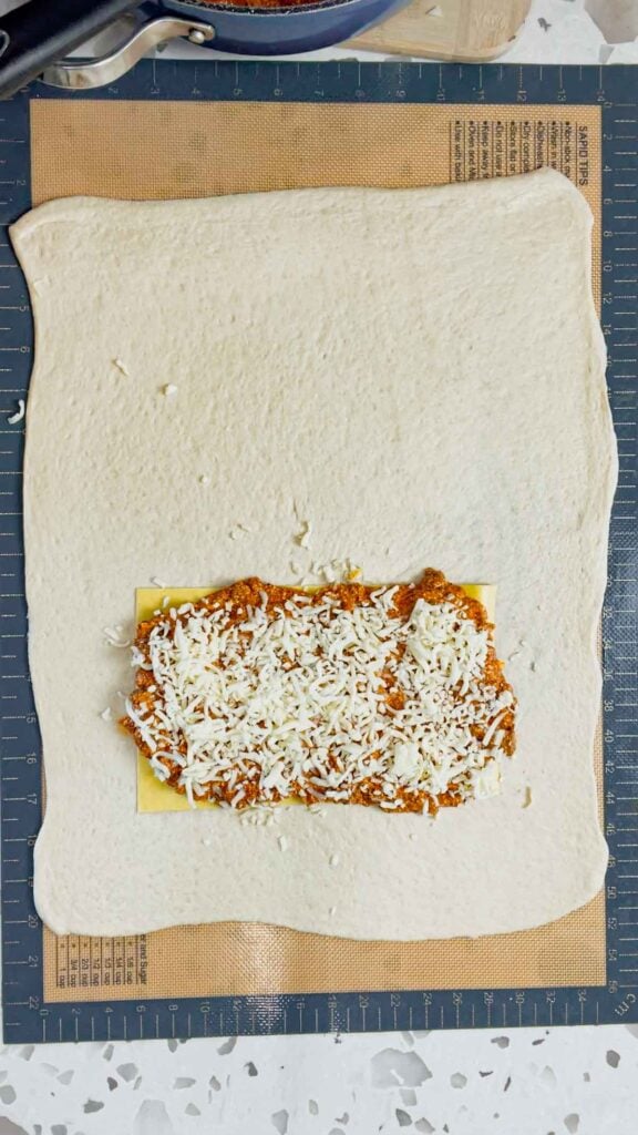 shredded mozzarella and meat sauce on top of lasagna pasta sheet on a rolled out pizza dough