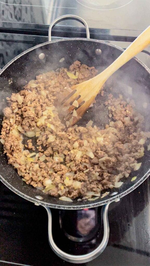 stirring garlic into cooked ground beef and diced onions in a skillet