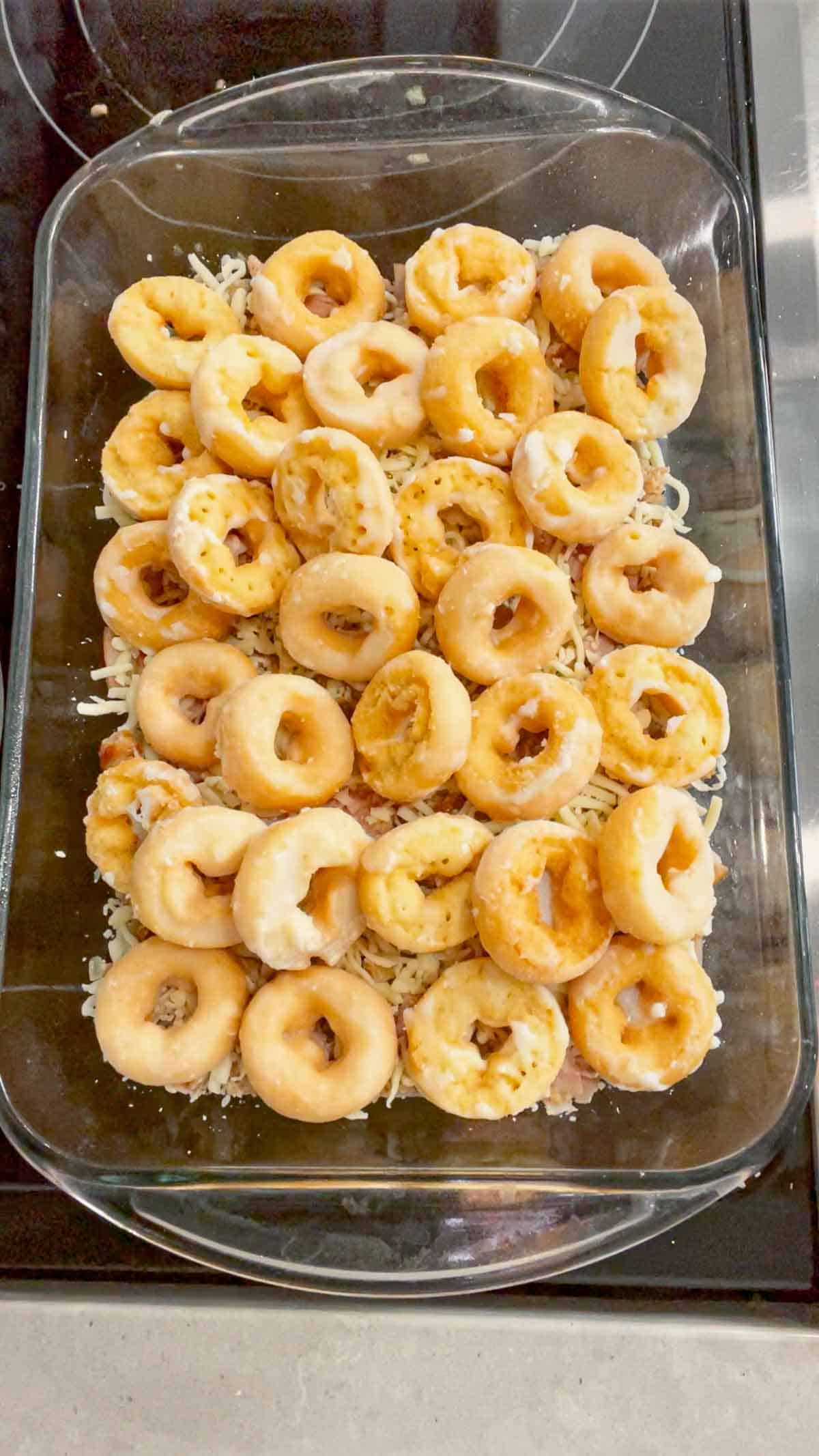 mini donuts on top of shredded cheese and cooked sausage meat in a baking dish