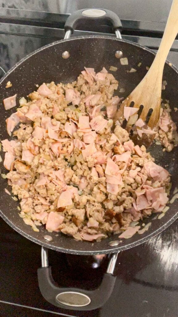 chopped ham being stirred with cooked sausage meat in a skillet