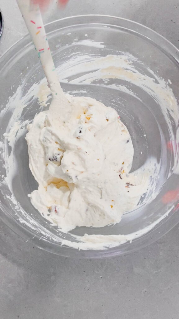 folding chopped timbits into cream cheese and cool whip mixture in a glass mixing bowl