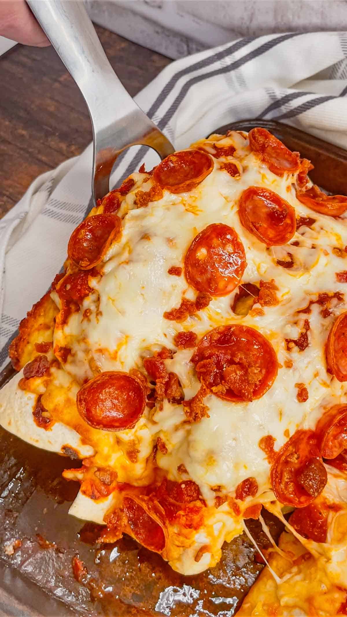 Pizza Enchiladas are a fun, family-friendly dinner recipe perfect for weeknights. Rolled flour tortillas are filled with ground beef, pepperoni, green peppers, onions and ricotta and baked with pizza sauce, mozzarella, pepperoni and bacon on top.