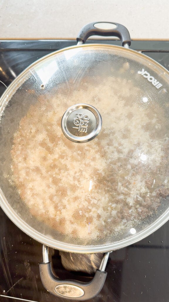 ground beef and rice cooking in a covered skillet