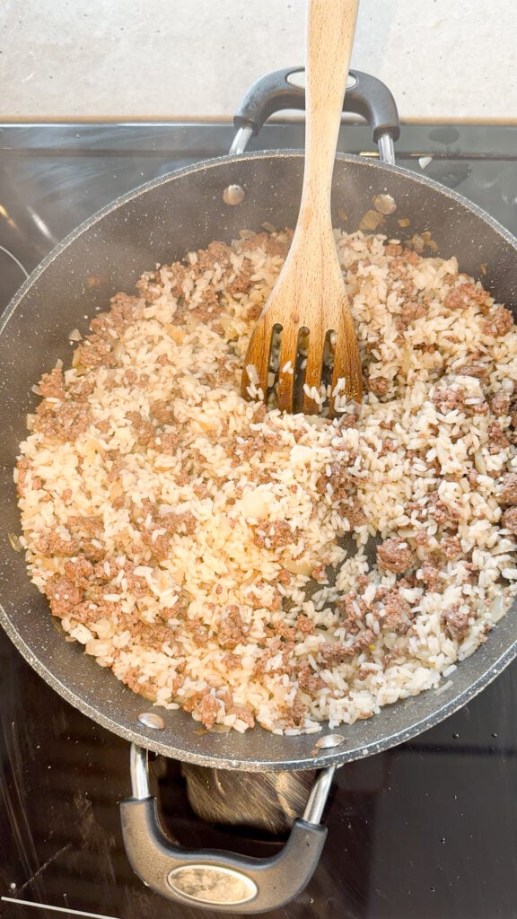 stirring cooked ground beef and rice together in a skillet