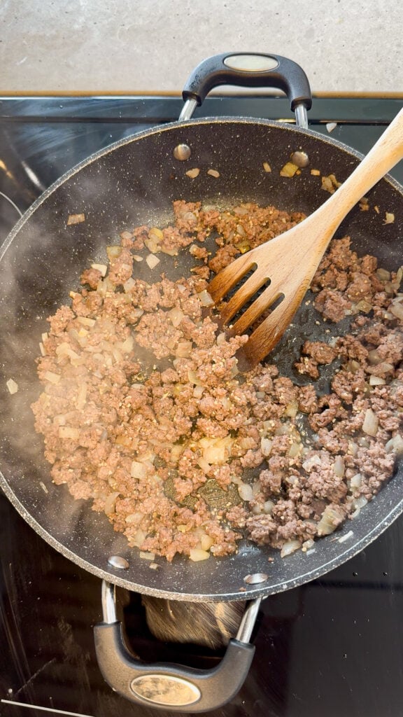 ground beef and diced onions cooking in a skillet