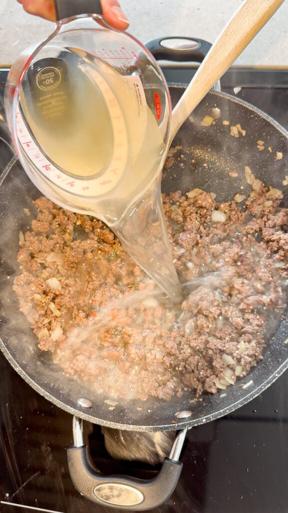 chicken broth added to a skillet with cooked ground beef