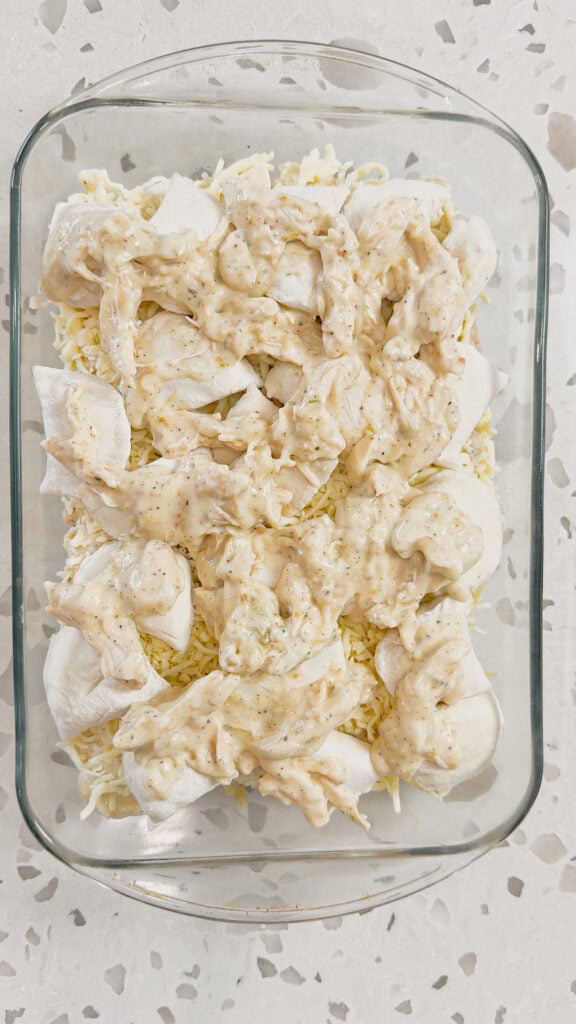 shredded chicken in alfredo sauce on top of frozen pierogies in a baking dish