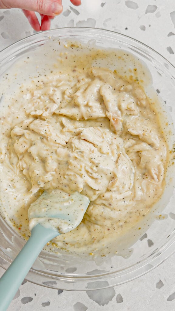 stirring alfredo sauce, italian seasoning, minced garlic and shredded chicken together in a bowl