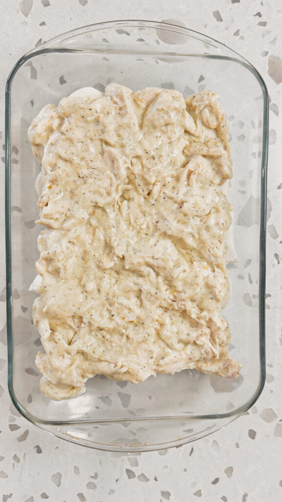 shredded chicken and alfredo sauce mixture on top of frozen pierogies in a glass baking dish