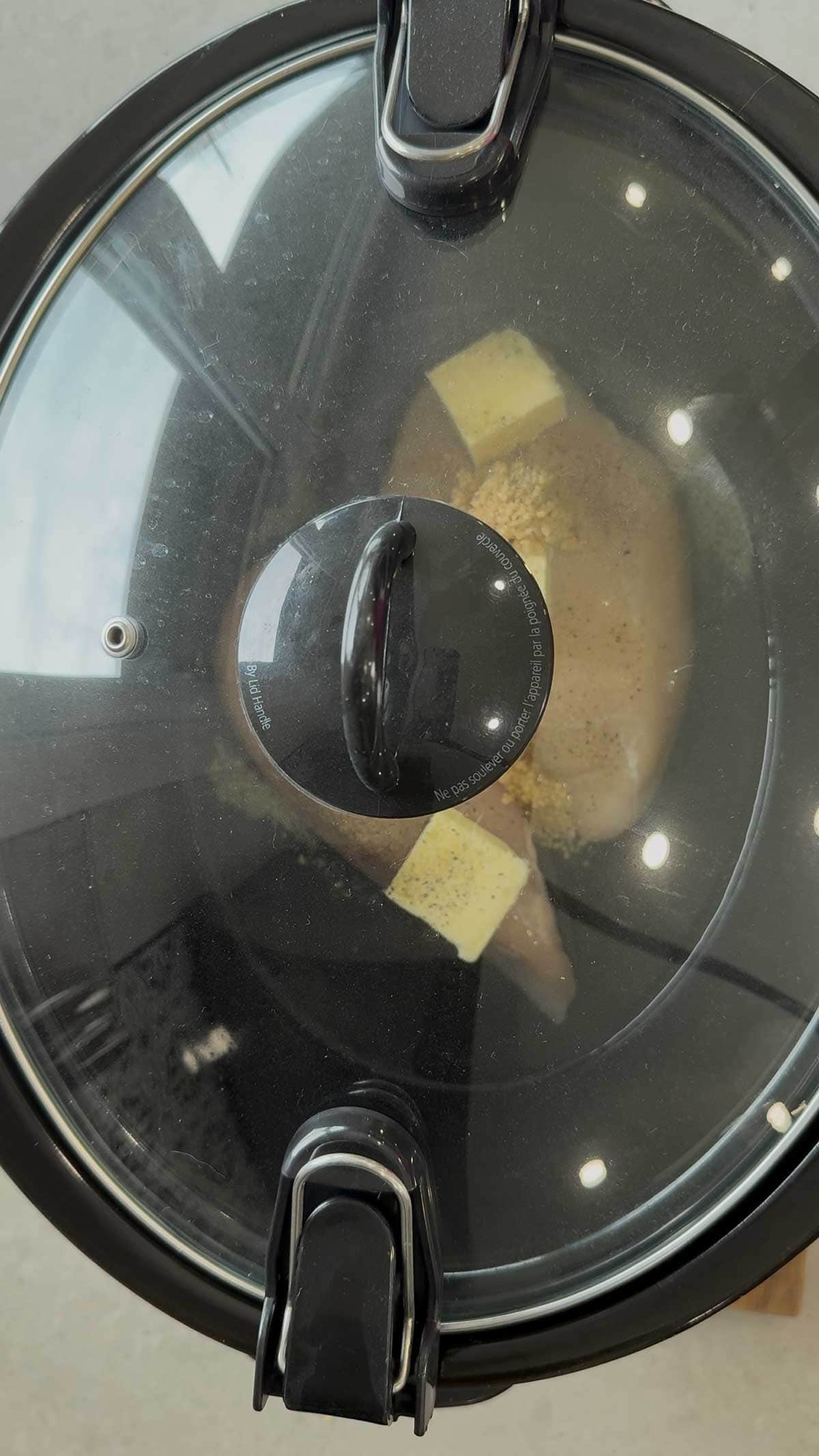 lid on crock pot containing raw chicken breasts, chicken broth, butter and chopped garlic