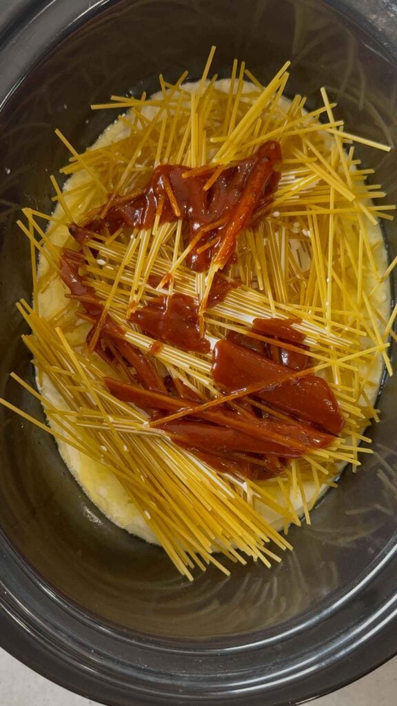 bbq sauce poured over uncooked spaghetti noodles and heavy cream in a slow cooker
