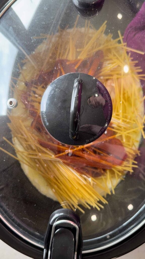 lid on crock pot containing spaghetti noodles, heavy cream and bbq sauce