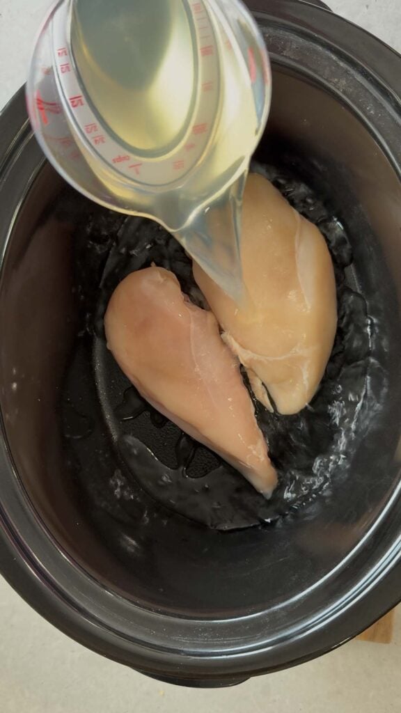 chicken broth poured over raw chicken breasts in a crock pot