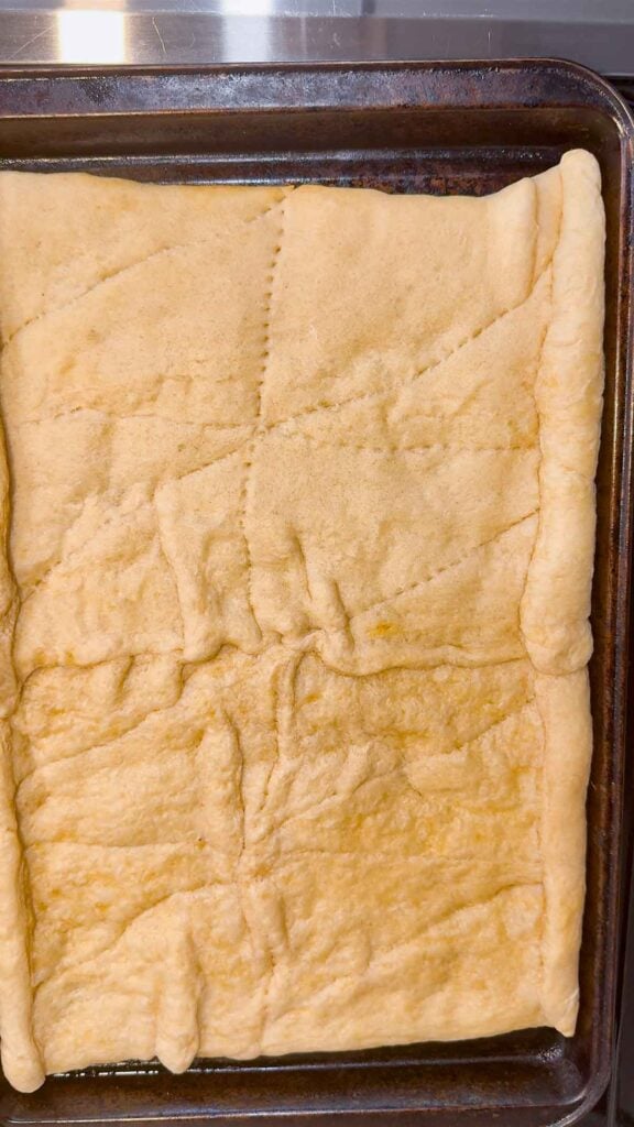 partially baked crescent roll dough pizza crust on a baking sheet