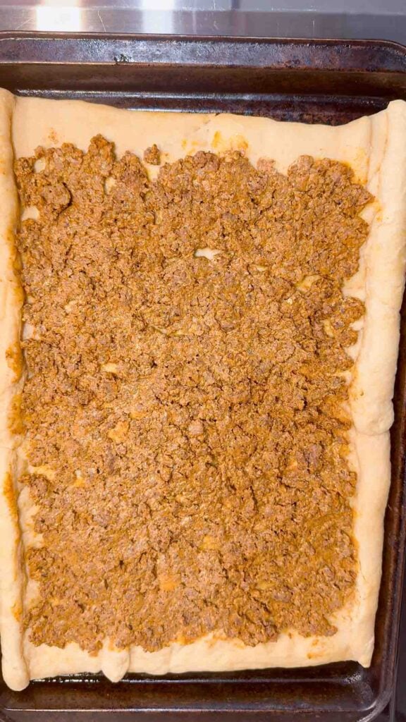cream cheese and ground beef taco meat mixture spread on a crescent dough pizza crust