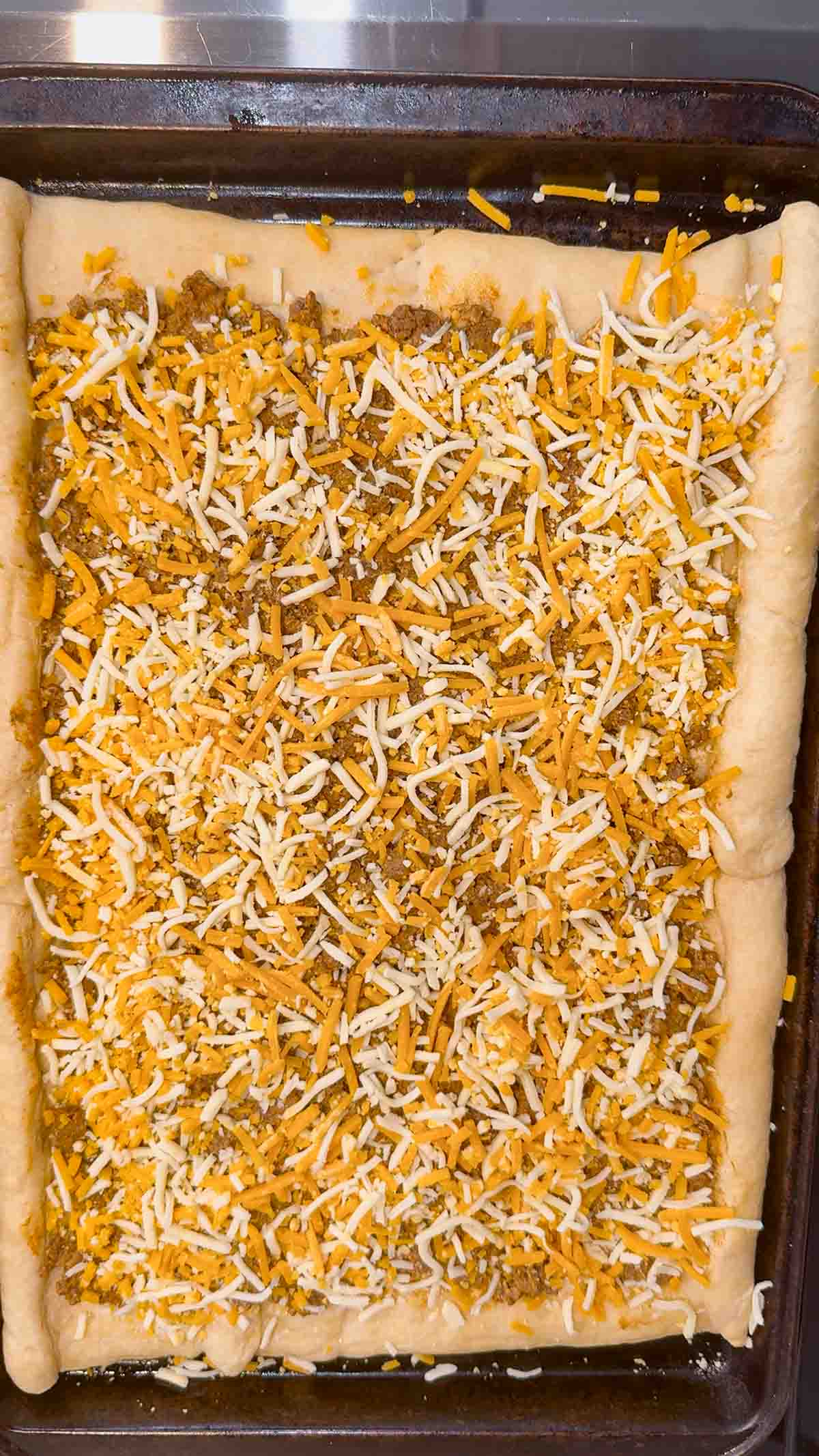 shredded nacho cheese on top of ground beef taco mixture on a crescent dough pizza crust